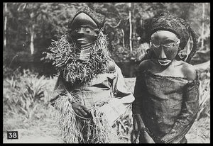 Youths (?) wearing the wooden masks Muyombo (left) and Nganga Ngombo (the diviner) (right) (the Muyombo mask is worn incorrectly in order to show it off better, it is normally worn with the face on top of the head) Youths (?) wearing the wooden masks Muyombo (left) and Nganga Ngombo (the diviner) (right) (the Muyombo mask is worn incorrectly in order to show it off better, it is normally worn with the face on top of the head)