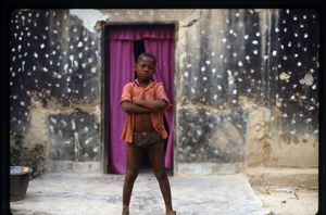 A boy, nephew of Jean-Pierre Bal'epou, wearing shorts and a shirt posing for the camera outside the front door or Bal'epou's house. A boy, nephew of Jean-Pierre Bal'epou, wearing shorts and a shirt posing for the camera outside the front door or Bal'epou's house.