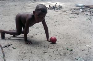 Close-up of a child crouching on all fours with a round red fruit on the ground just in front of him or her. Close-up of a child crouching on all fours with a round red fruit on the ground just in front of him or her.
